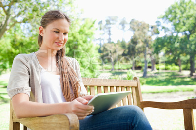 Smiling woman using a tablet on a park bench