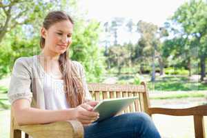 Smiling woman using a tablet on a park bench