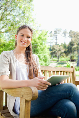 Smiling woman sitting on a bench with her tablet computer