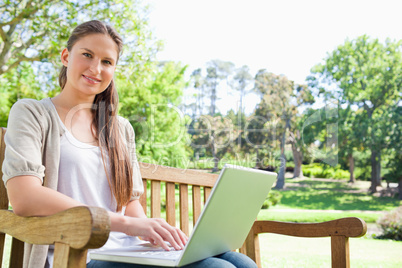 Smiling woman with a laptop on a park bench