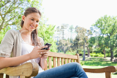 Smiling woman reading text message on a park bench