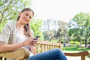 Smiling woman writing a text message on a park bench