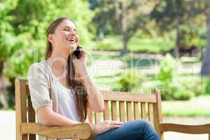 Laughing woman on her cellphone on a park bench