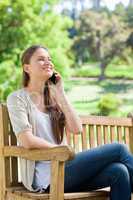 Smiling woman sitting with her cellphone on a park bench