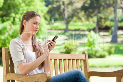 Woman writing a text message on her cellphone while on a park be