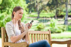 Woman writing a text message on her cellphone while on a park be