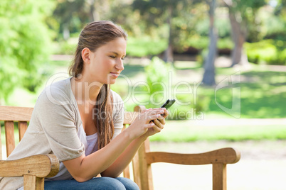 Woman reading a text message on a park bench