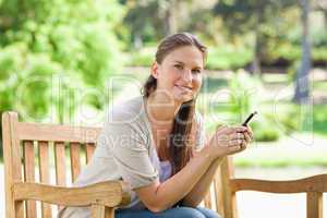 Smiling woman sitting on a park bench with her cellphone