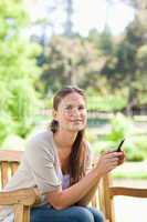 Smiling woman holding her cellphone while on a park bench