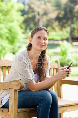 Woman with her cellphone sitting on a park bench