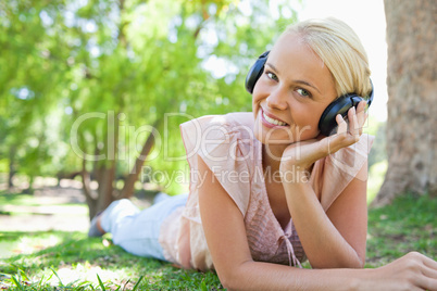 Smiling woman lying on the lawn while wearing headphones