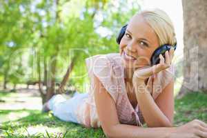 Smiling woman lying on the lawn while wearing headphones