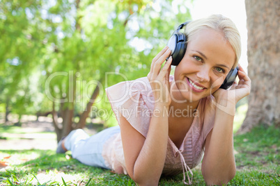 Smiling woman lying on the grass while listening to music