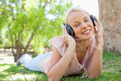 Woman wearing headphones while lying on the lawn