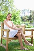 Smiling woman with her legs crossed  sitting on a park bench