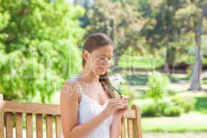 Smiling woman with a flower sitting on a park bench