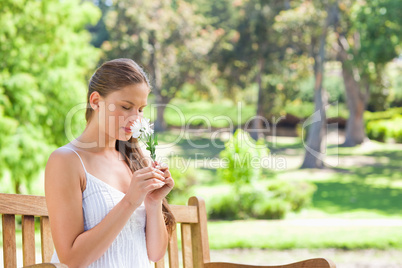 Woman smelling a flower while sitting on a park bench