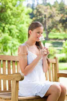 Smiling woman smelling on a flower while sitting on a park bench