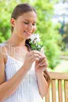 Smiling woman on a park bench smelling on a flower