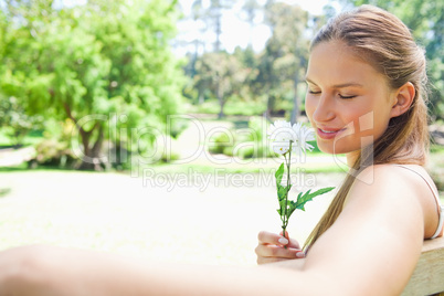 Side view of a woman on a park bench smelling a flower