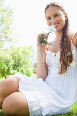 Smiling woman with a flower sitting on the lawn