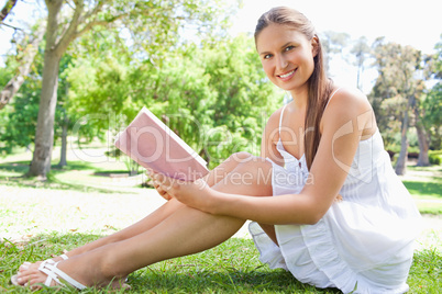 Side view of a smiling woman sitting on the lawn with a book