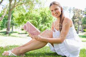 Side view of a smiling woman sitting on the lawn with a book