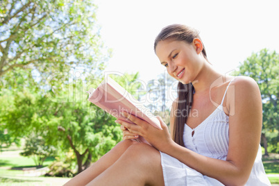 Side view of a smiling woman on the lawn reading a book