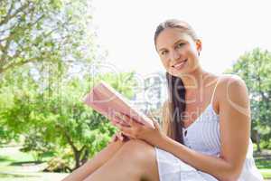 Side view of a smiling woman with a book on the lawn