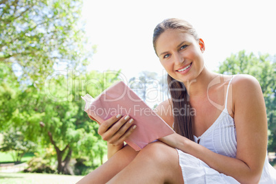Side view of a smiling woman with a novel in the park