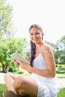 Side view of a smiling woman sitting on the lawn with a tablet c