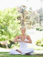 Smiling woman sitting in the park in a yoga position