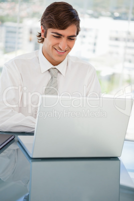 Smiling young businessman is on his laptop