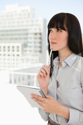 A woman with a notepad and pen against her chin as she thinks