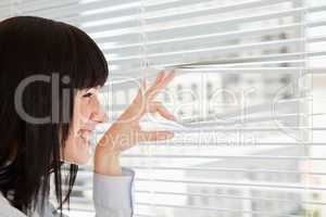 A smiling woman looks out through her blinds