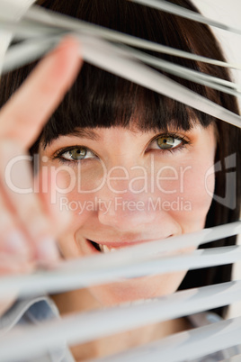 Close up of woman looking through blinds into the camera