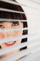 A woman looking forward through her blinds without moving them