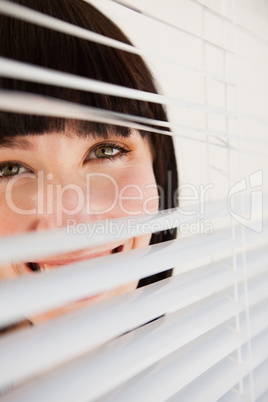 A woman looking through blinds she has opened slightly