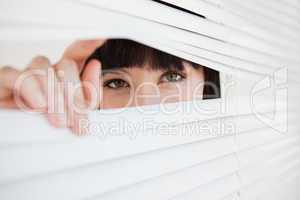 A woman opening a part of closed blinds with her fingers