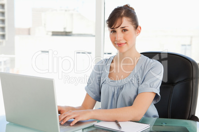 A smiling employee sits at her desk with her laptop