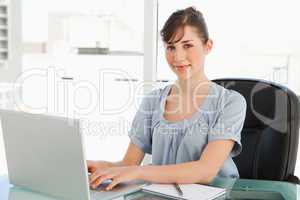 A smiling employee sits at her desk with her laptop