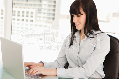 A smiling business woman looks at her laptop as she types