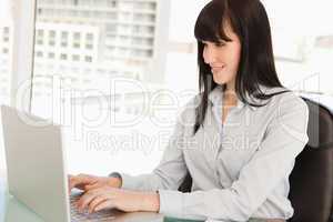 A smiling business woman looks at her laptop as she types