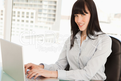 A woman looks at the camera as she types on her laptop