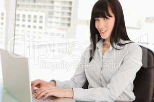 A woman looks at the camera as she types on her laptop
