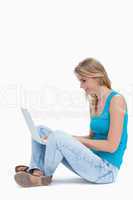 A side view of a woman sitting on the ground typing on a laptop