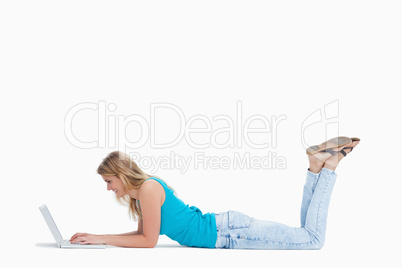 A woman lying on the floor with her legs up is typing on her lap