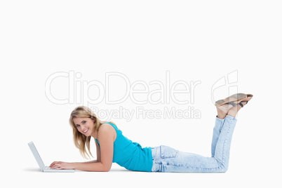 A smiling woman lying on the floor with her laptop