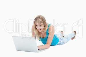 A surprised woman looking at a laptop is lying on the floor