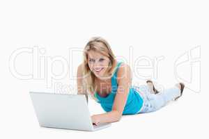 A smiling woman is lying on the floor with a laptop in front of
